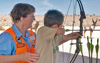 Become a Wildlife Conservation Volunteer. (Photo of archery instructor helping youth). New Mexico Department of Game and Fish